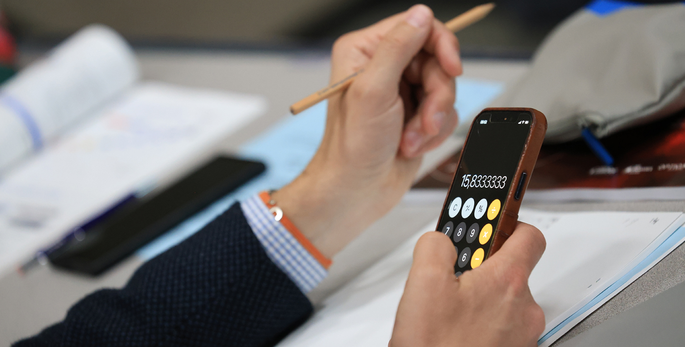 Person holding a cell phone open to the calcuator app and holding a pencil