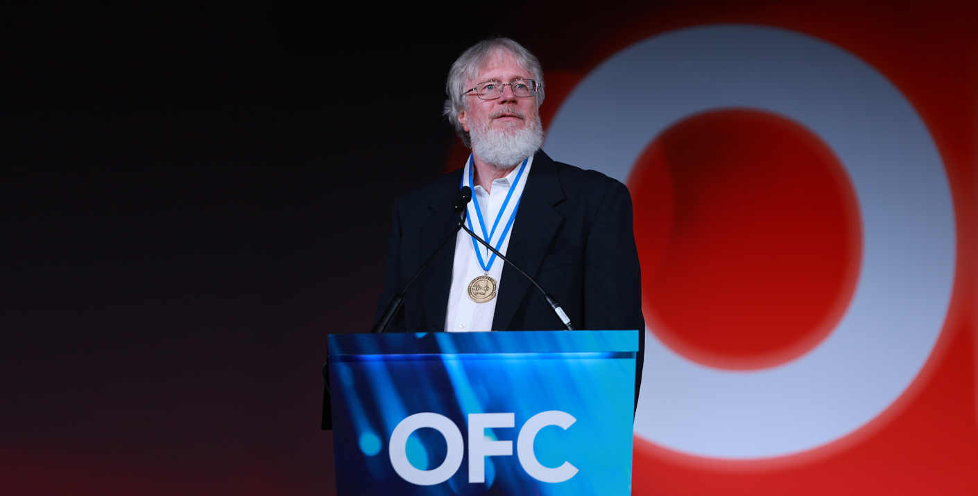 A man standing behind a blue podium with OFC on it speaking.
